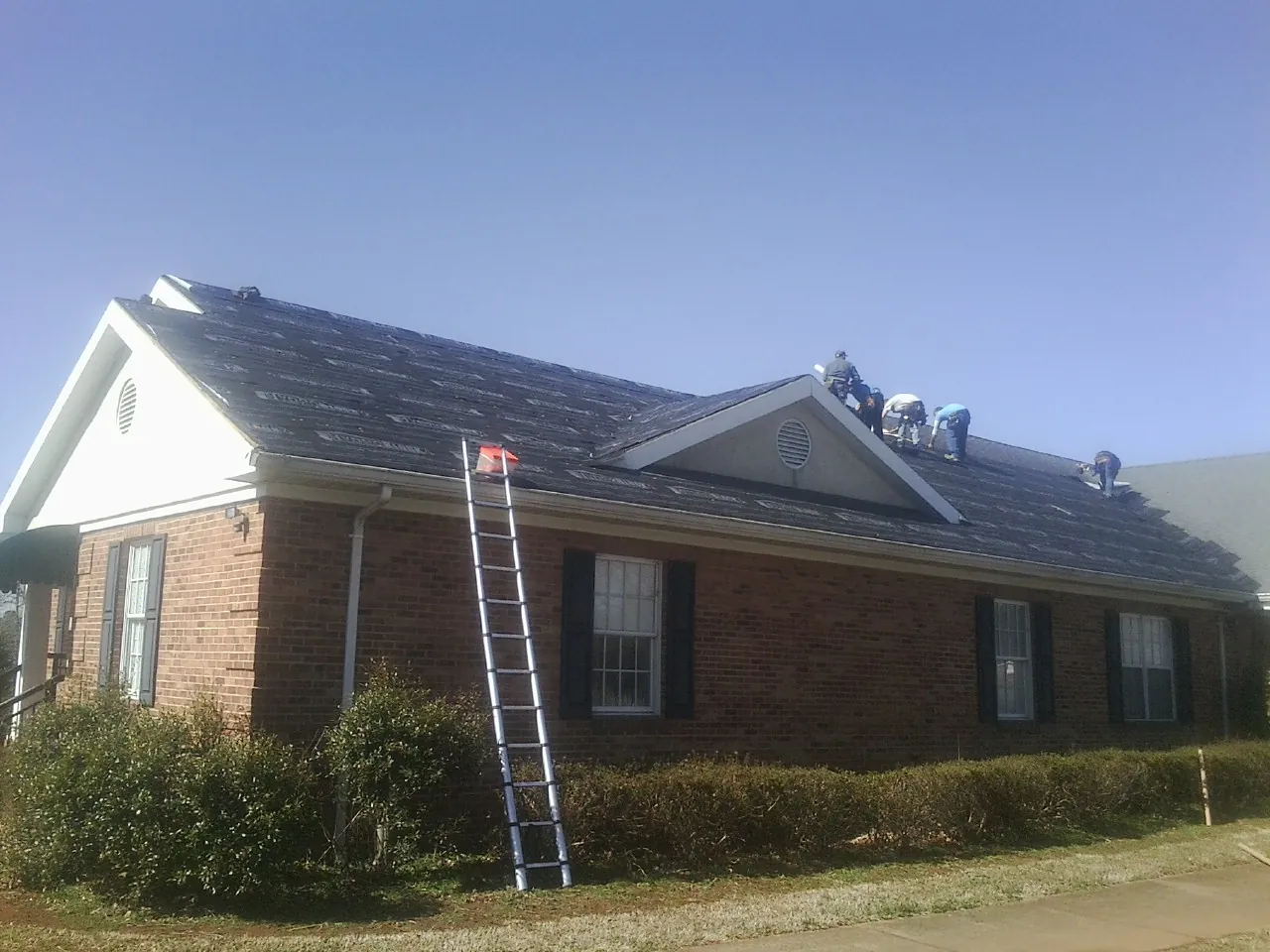Crew tearing shingles off a brick ranch roof with a ladder set — Emergency Roof Repair work by our crew in Hamler