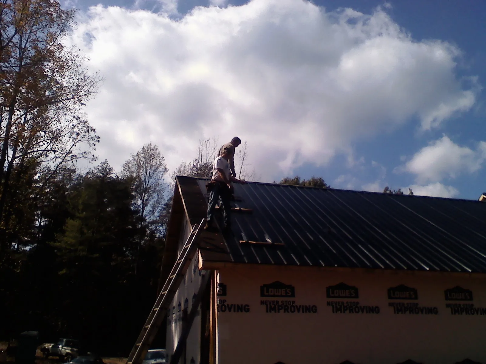 Roofer fastening dark metal panels high against a cloudy sky, from a Roof Inspection job in Hamler