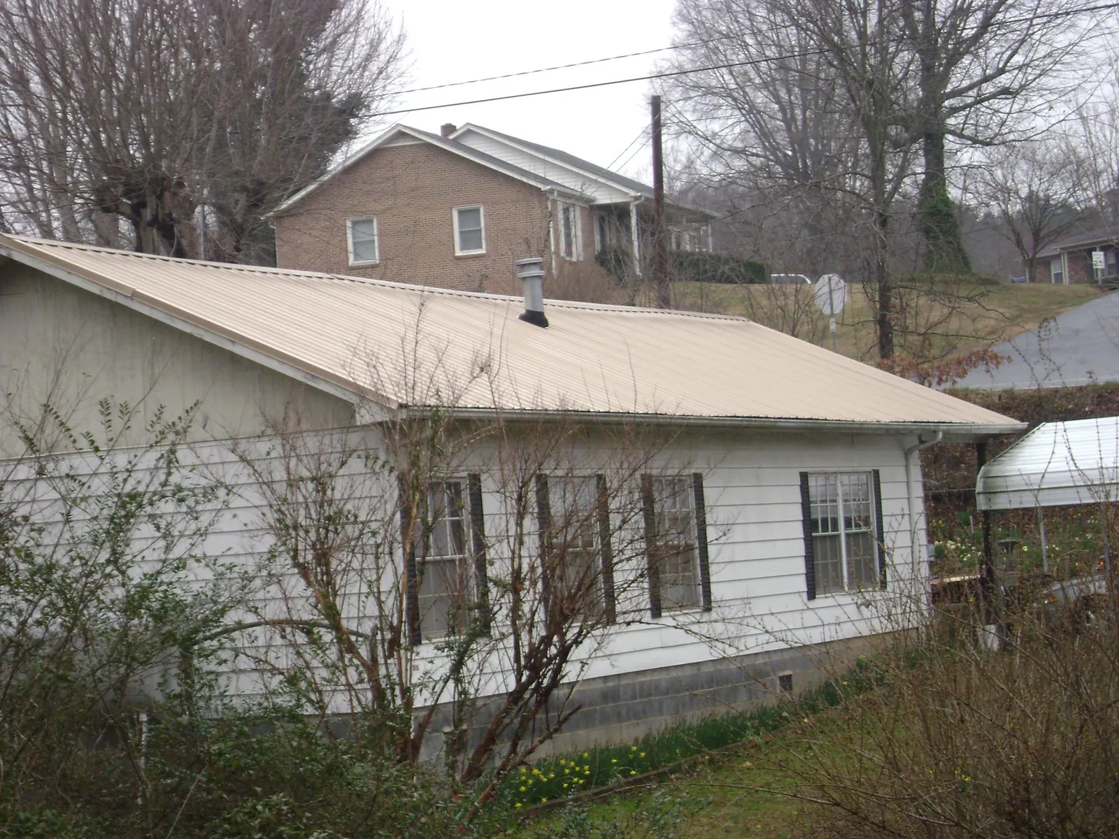Tan metal roof on a white sided house set into a hillside — Commercial Roofing by Roofing Brothers in Hamler