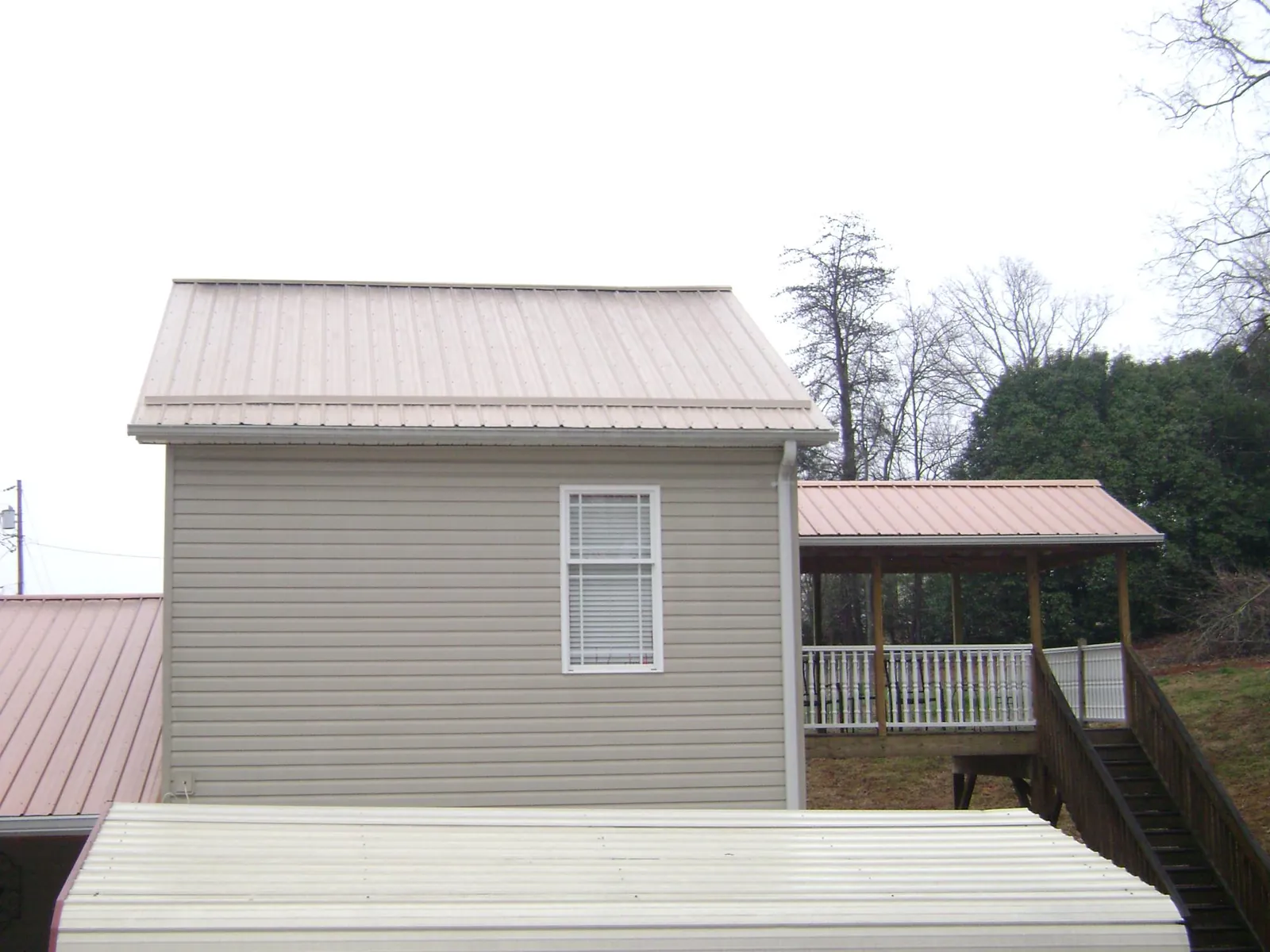 Tan metal roofs on a two story addition and attached porch, from a Roof Replacement job in Hamler